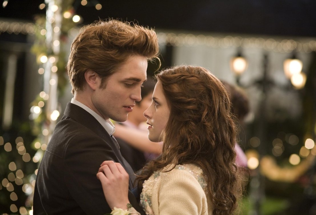 Robert Pattinson as Edward and Kristen Stewart as Bella, sharing an intense eye contact while slow dancing in the middle of a gazebo with string lights in a scene from 'Twilight'.