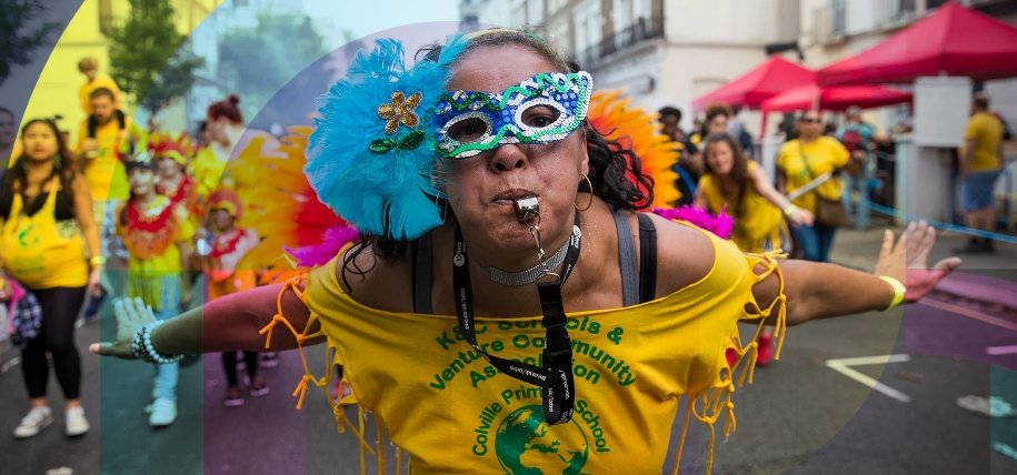 A performer in a yellow top and a sequined masquerade mask blows a whistle with outstretched arms during a parade at the Notting Hill Carnival.
