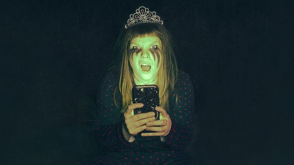 Alfrun Rose wears a tiara and smeared makeup while looking shocked at a glowing phone in new play Dead Air at Greenwich Theatre