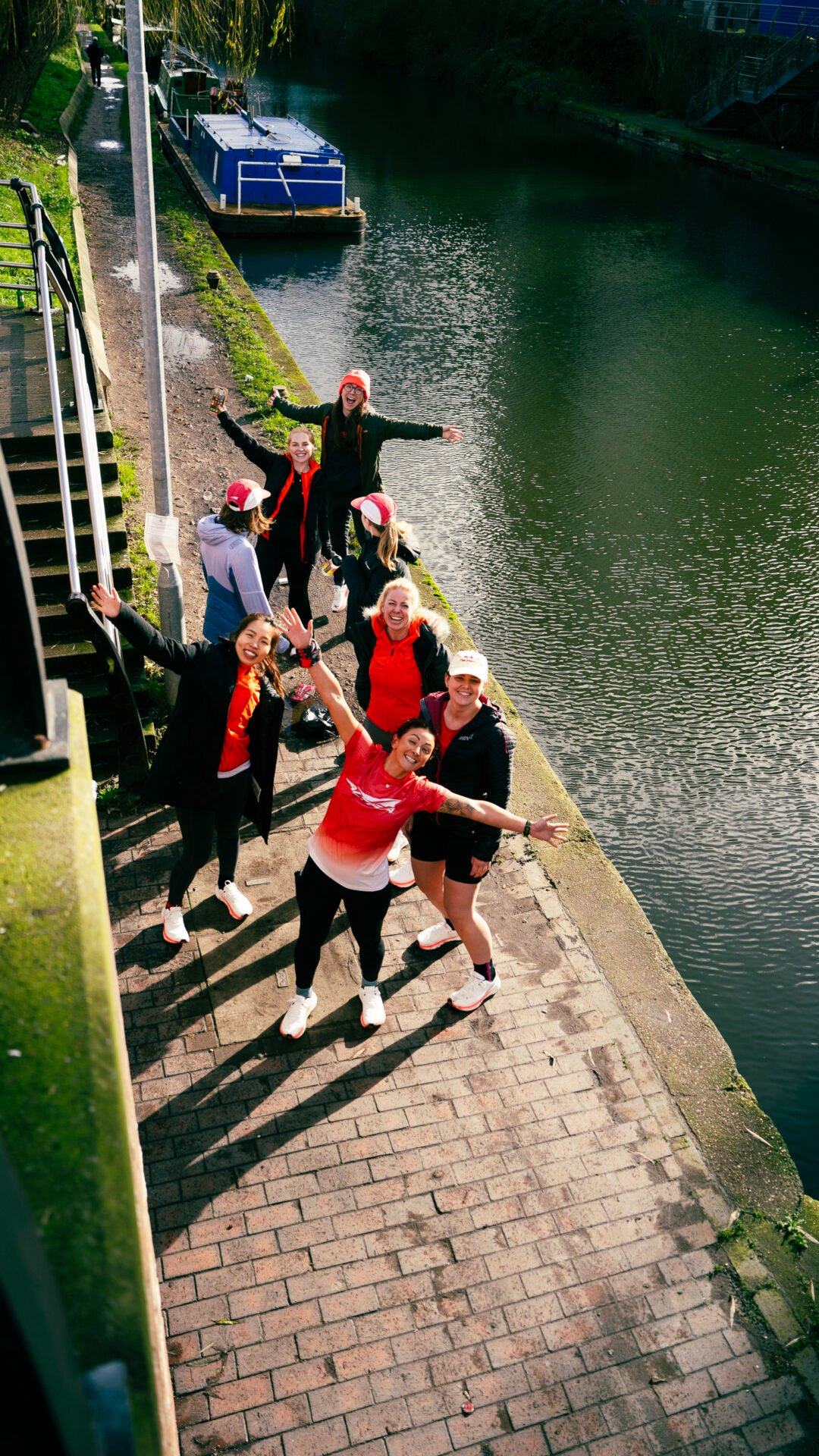 A group of women from the Altra She Runs Free team posing alongside a canal. One woman wears a red top, with her arms outstretched, posing for the photograph