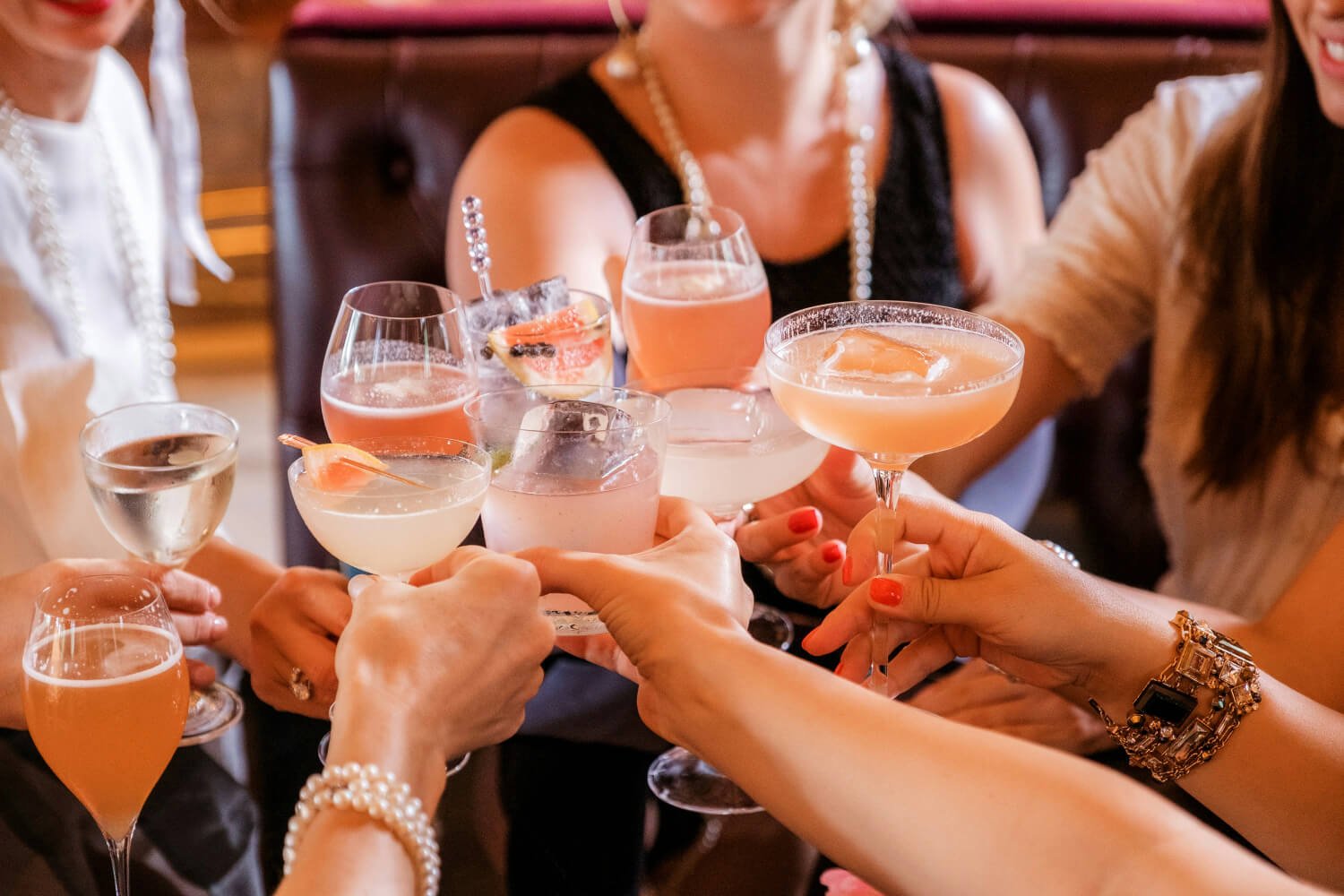 Group of women clinking glasses with cocktails in a social setting, celebrating together