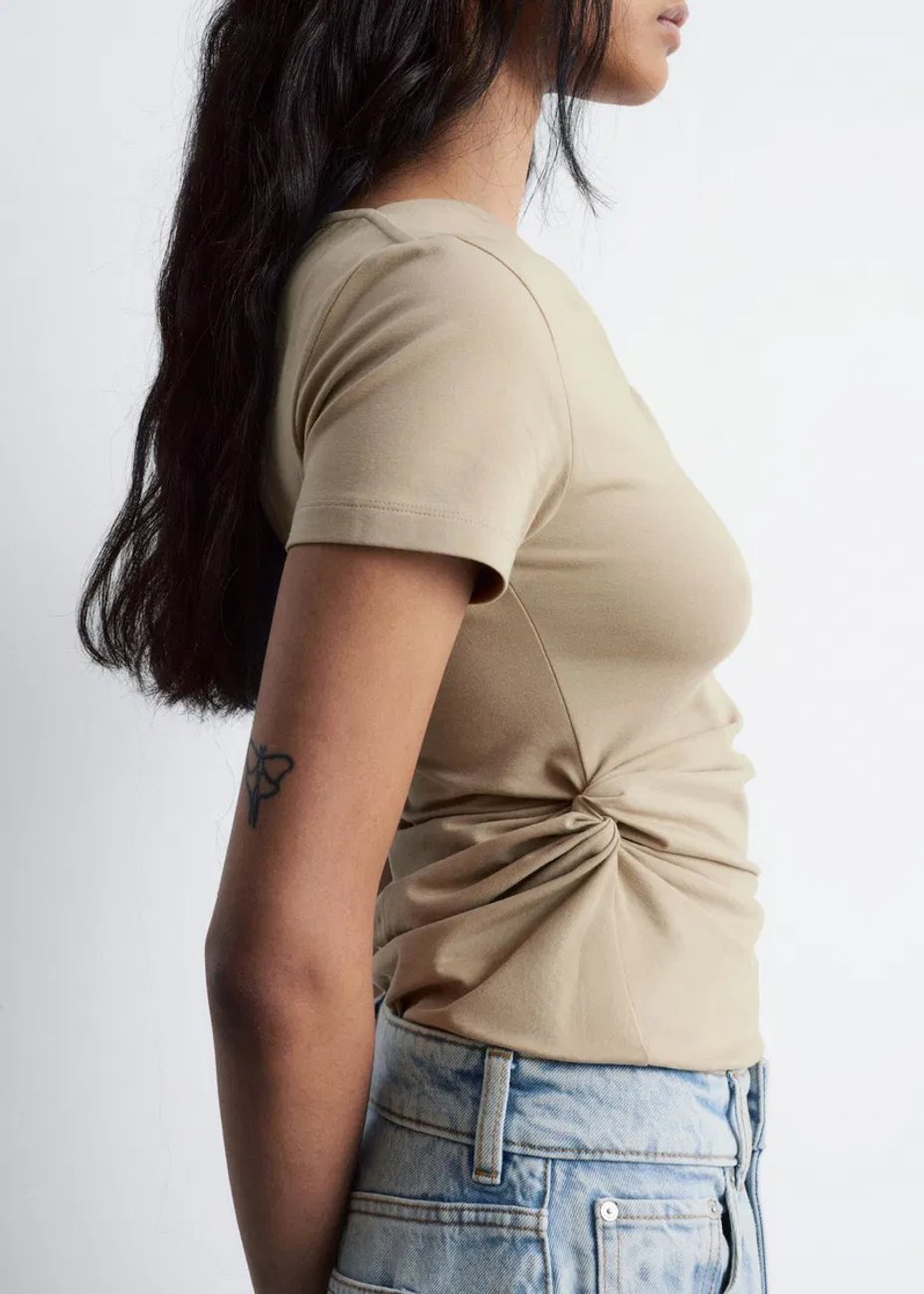 Side view of a model wearing & Other Stories Twist Detail T-shirt in khaki green, a short-sleeve shirt with a twist detail at the front