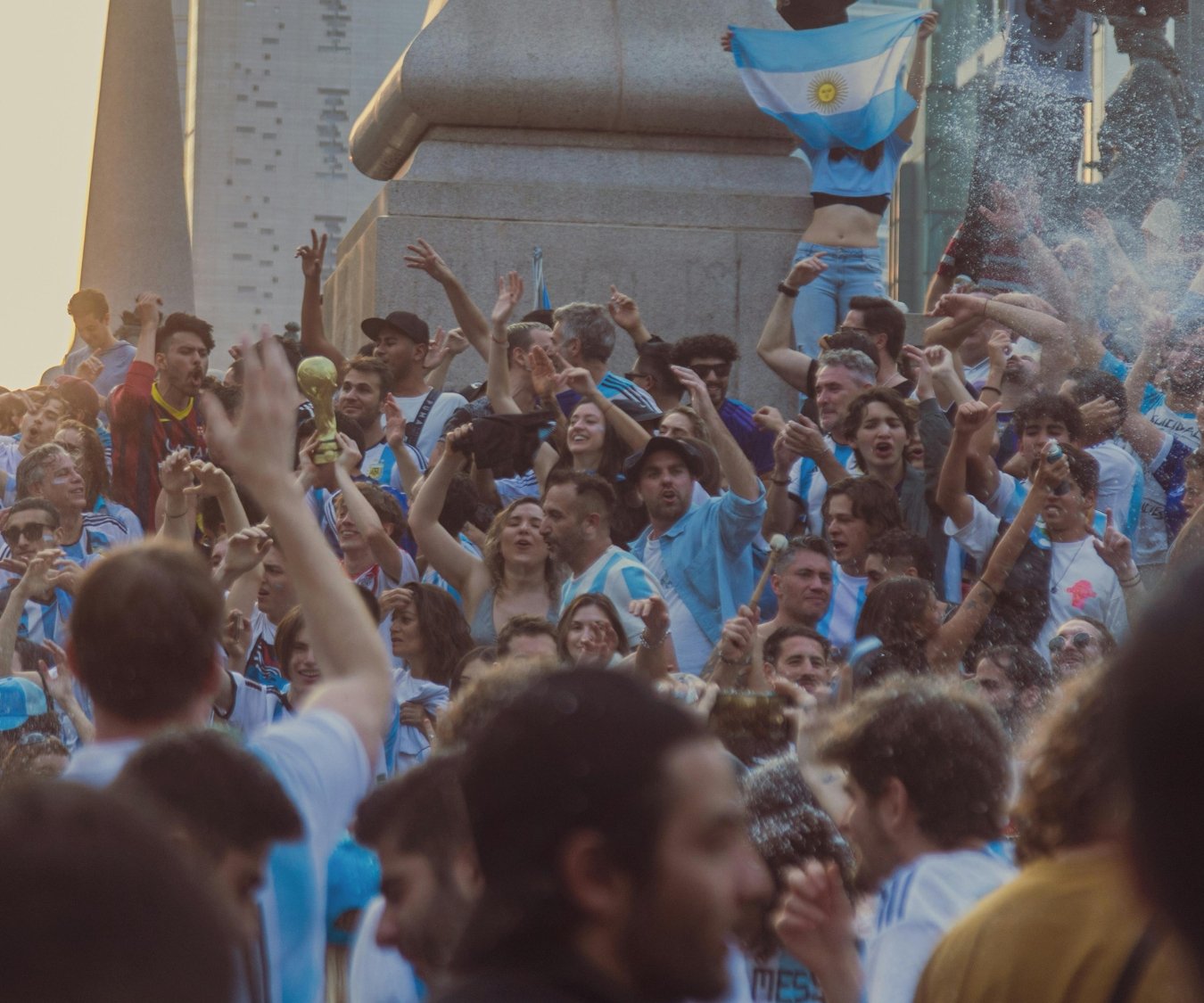 Argentina football fans celebrate in a crowded city square, waving national flags and holding a replica World Cup trophy ahead of Argentina's FIFA World Cup 2026 campaign as the country introduces a stadium ban for parents with unpaid child support debts