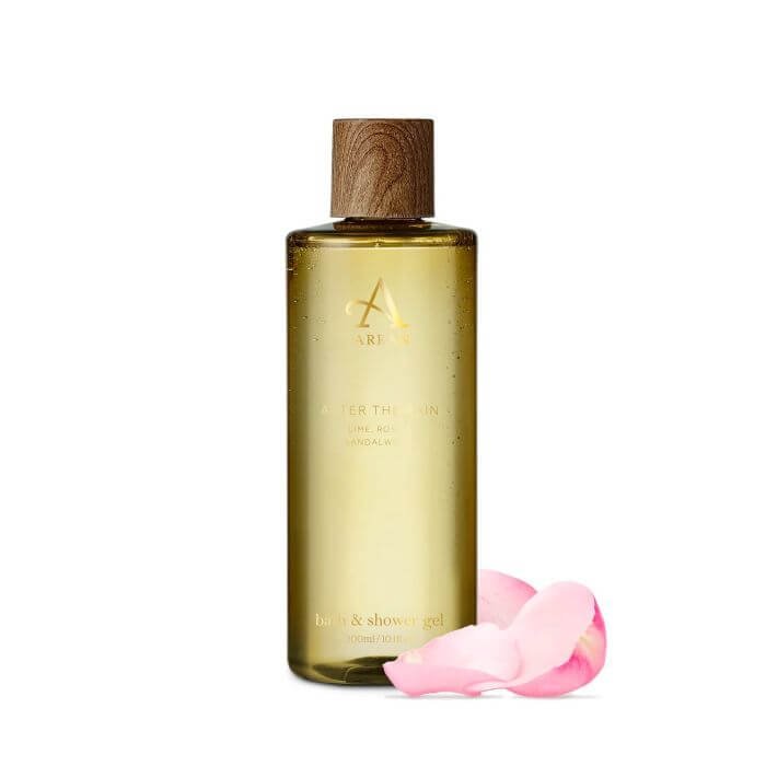 A bottle of Arran After The Rain shower gel with a wooden cap next to pink rose petals
