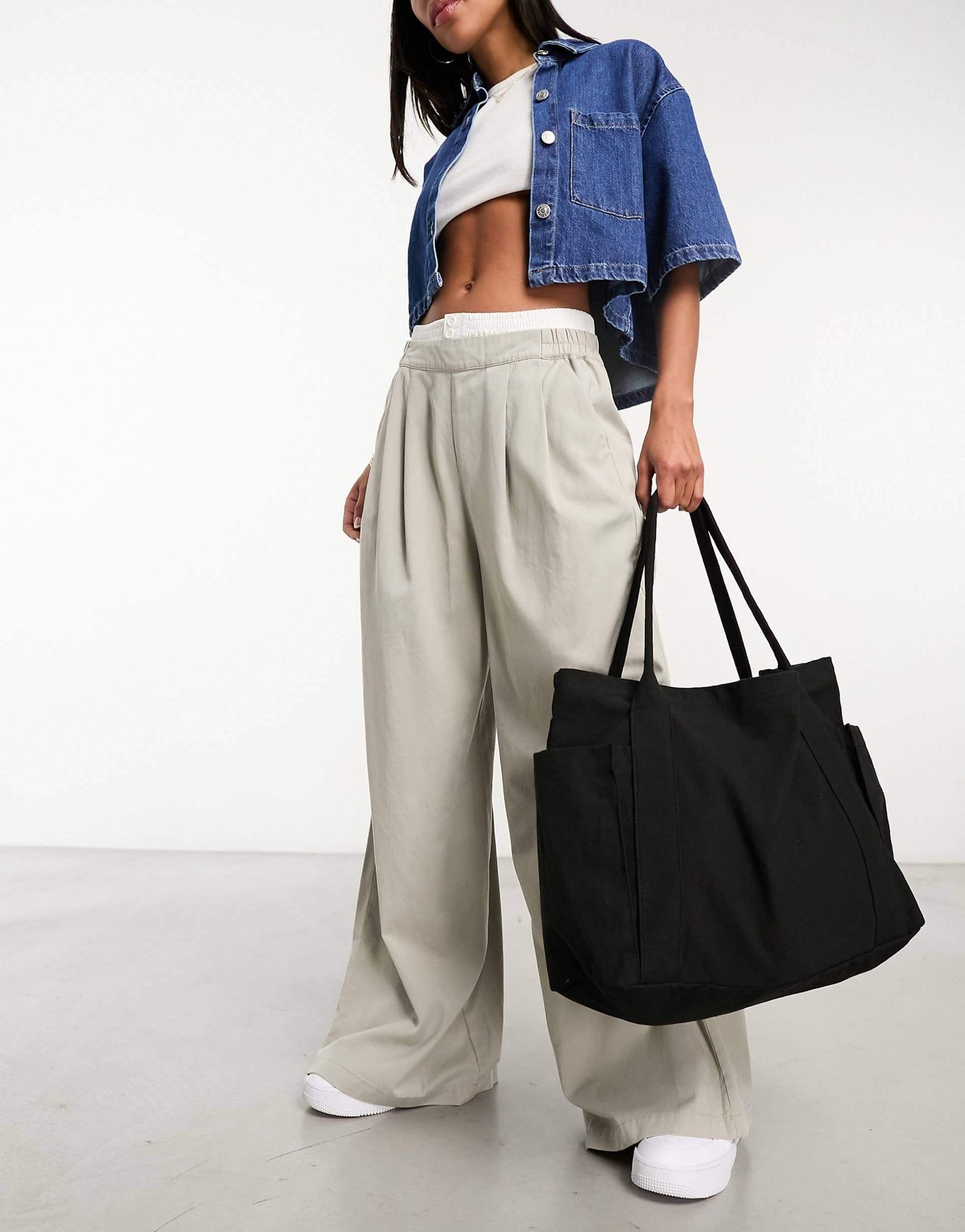 Model holding ASOS Design Oversized Heavyweight Canvas Tote Bag in black, wearing light trousers, a denim jacket, and white t shirt