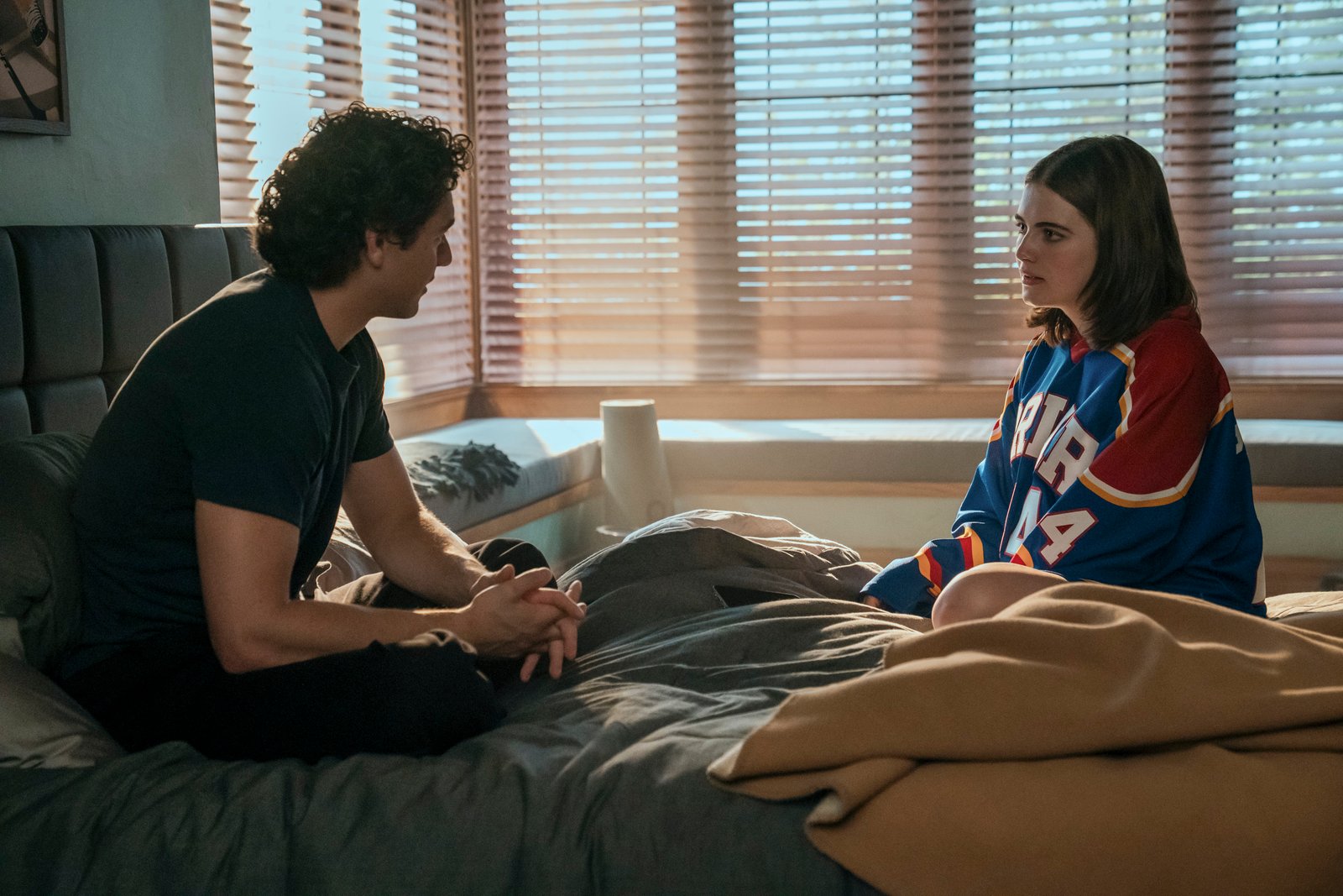Belmont Cameli as Garrett and Ella Bright as Hannah sitting across from each other in bed in a scene from 'Off Campus'.