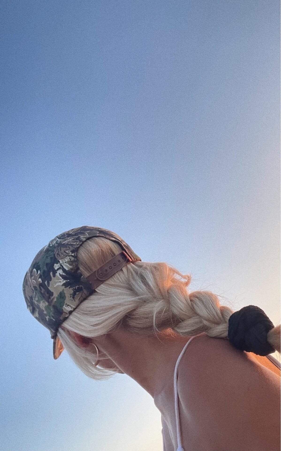 A woman with blonde hair in a braid, wearing a patterned cap, looking towards the sky