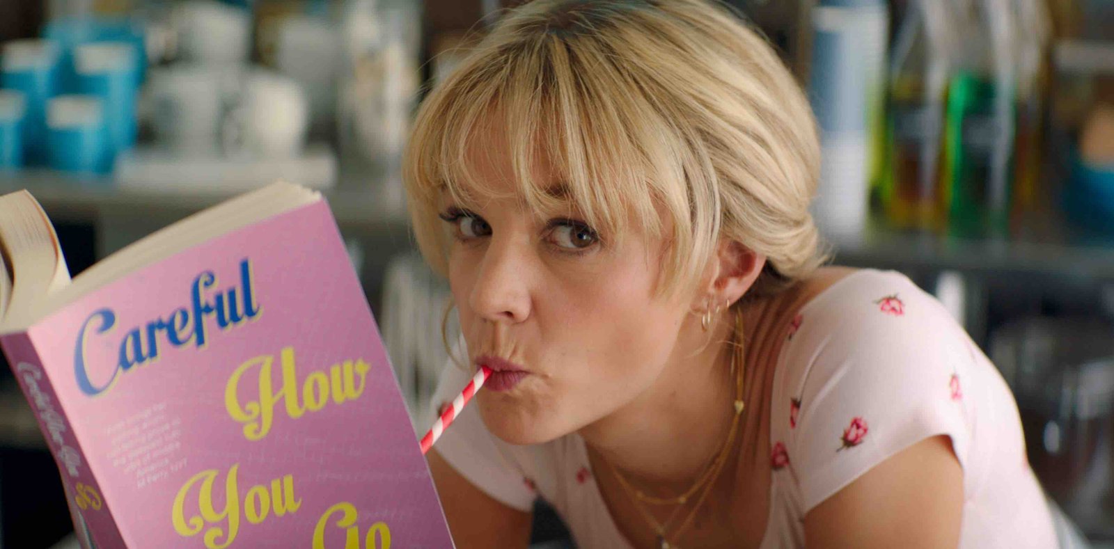 Carey Mulligan is sipping out of a straw while reading a book in a scene from 'Promising Young Woman'.