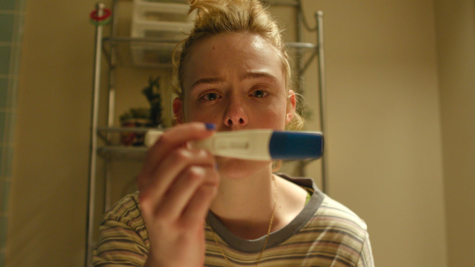 Elle Fanning as Margo has a concerned expression while staring at a positive pregnancy test in a scene from 'Margo's Got Money Troubles'.