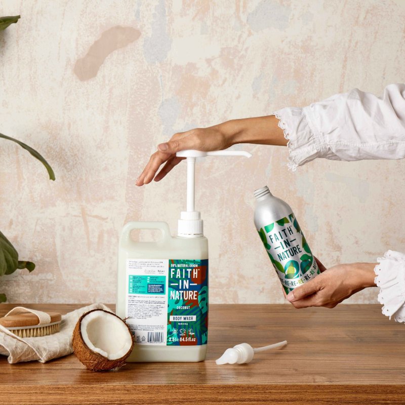 A hand pours body wash into a pump from a refillable aluminium bottle, with a coconut nearby