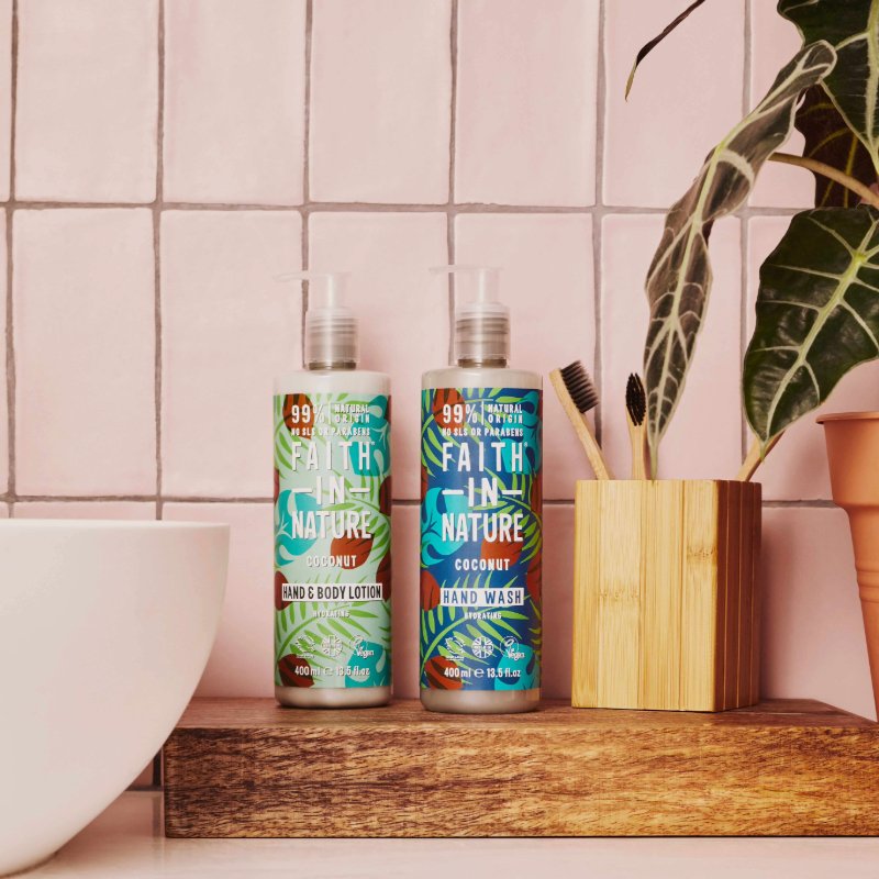 Coconut hand wash and body lotion by Faith in Nature on a wooden shelf next to a plant