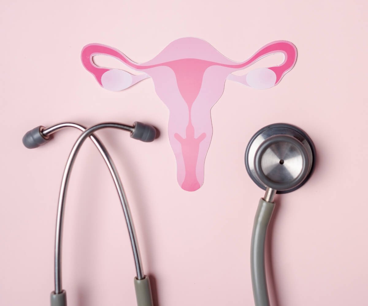 A pink illustration of the female reproductive system placed above a stethoscope on a pale pink background, representing women’s hormonal health and the renaming of PCOS to PMOS
