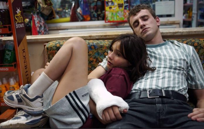 Frankie Corio as Sophie lying on Paul Mescal's lap as his character Calum falls asleep and wraps his right arm with a cast around her in a scene from 'Aftersun'.
