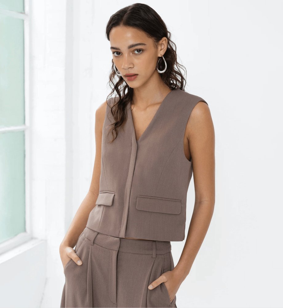 Model wearing the French Connection Vienna V Neck Pocket Waistcoat in taupe brown. Tailored sleeveless waistcoat with V-neckline and front pocket details styled with matching trousers for a modern workwear look