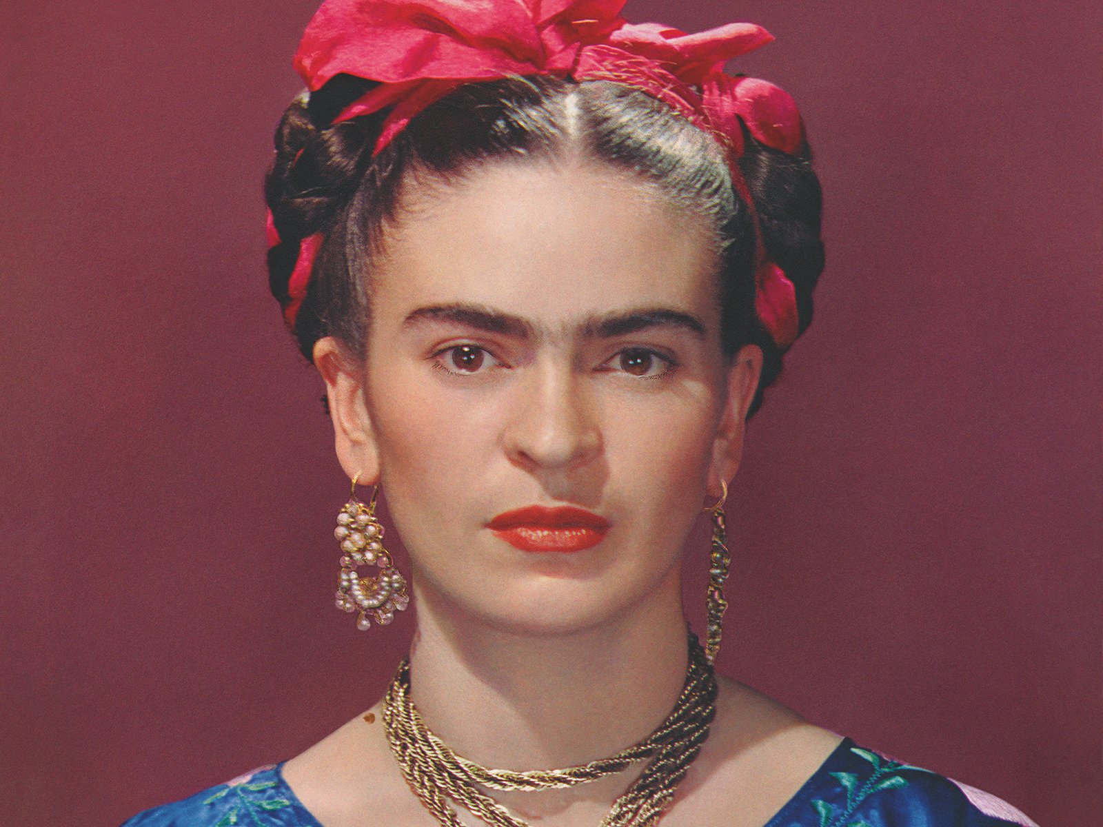 Detailed portrait of Frida Kahlo with braided hair, a bright pink head ribbon, and ornate gold jewelry against a dark red background.