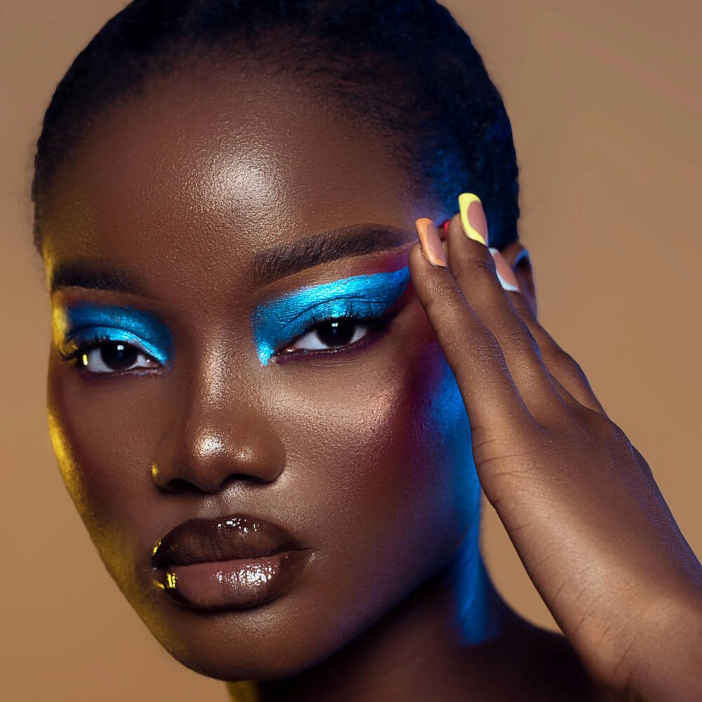 Close-up of a person with bold blue festival makeup and glossy lips gesturing with a hand near the face