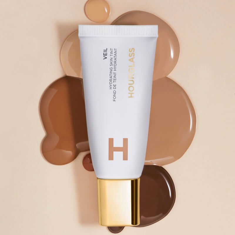 Hourglass Veil Hydrating Skin Tint tube beside smooth swatches of various shades