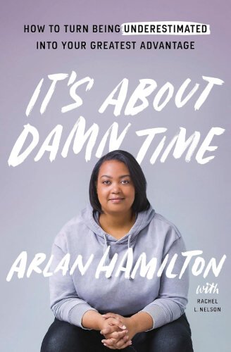 Cover of “It’s About Damn Time” by Arlan Hamilton and Rachel L. Nelson, featuring Arlan Hamilton seated at the centre on a light lilac background, wearing a light grey hoodie and smiling softly, with the title and author names in slanted white capital letters.