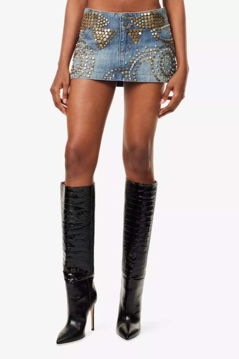 A model wearing Jaded London stud-embellished denim mini skirt with a fitted silhouette and tall black heeled boots