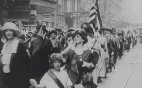 Archival footage of a historic women's suffrage march with participants carrying flags
