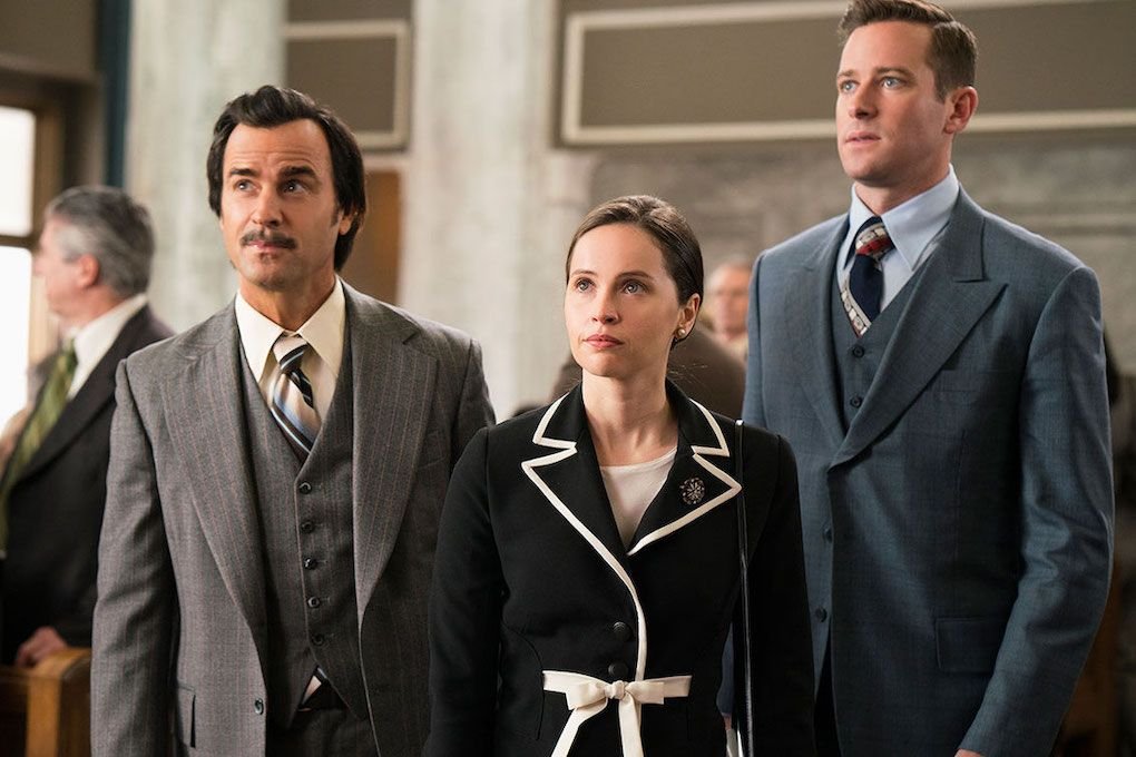 Justin Theroux as Mel Wulf, Felicity Jones as Ruth Bader Ginsburg, and Armie Hammer as Martin D. Ginsburg wearing suits and standing side-by-side in a scene from 'On the Basis of Sex'.