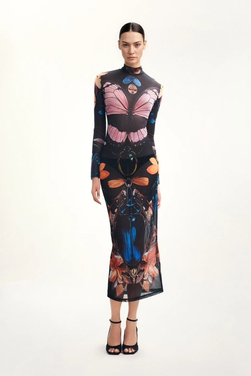 Model wearing a sheer long-sleeve midaxi dress featuring vibrant butterfly and floral prints