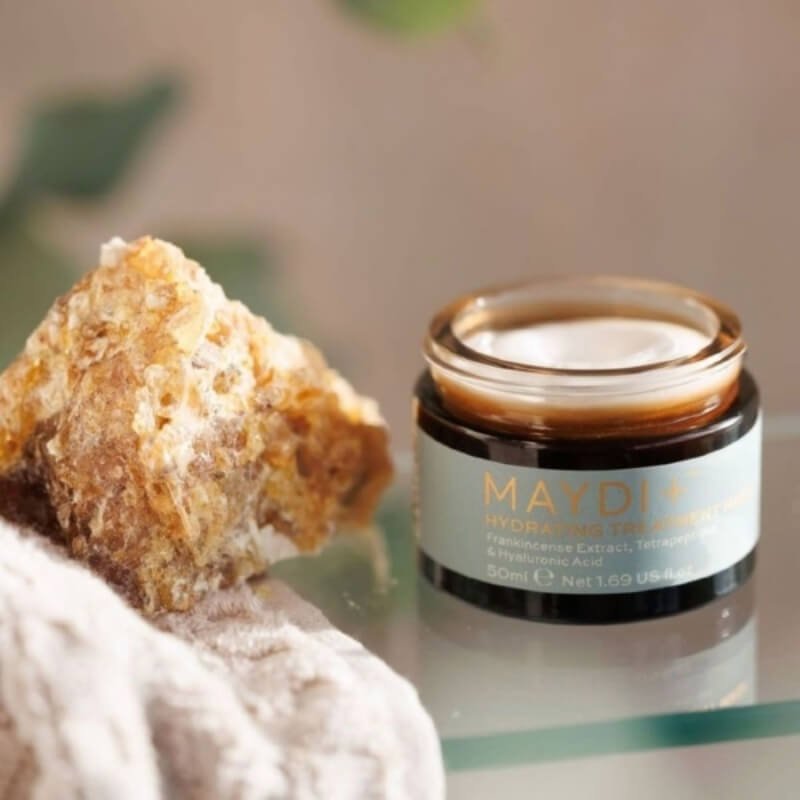 A jar of MAYDI+ hydrating treatment mask next to a natural crystal and a soft towel