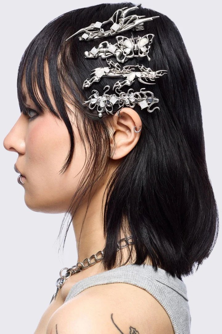 A profile view of a person with black hair styled with decorative hair clips, wearing a silver chain necklace and a grey sleeveless top