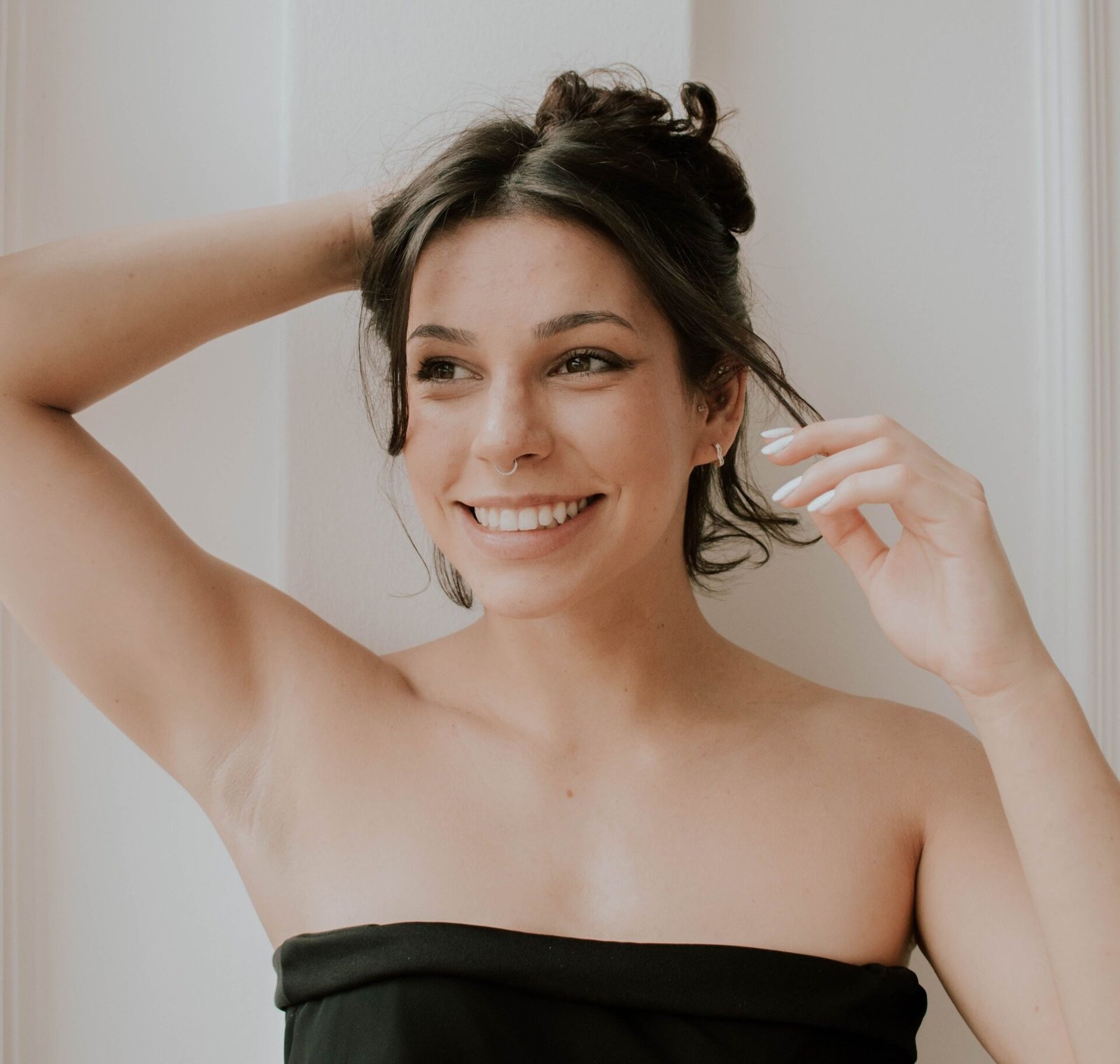 A woman smiling while running her fingers through her short hair, wearing a strapless top