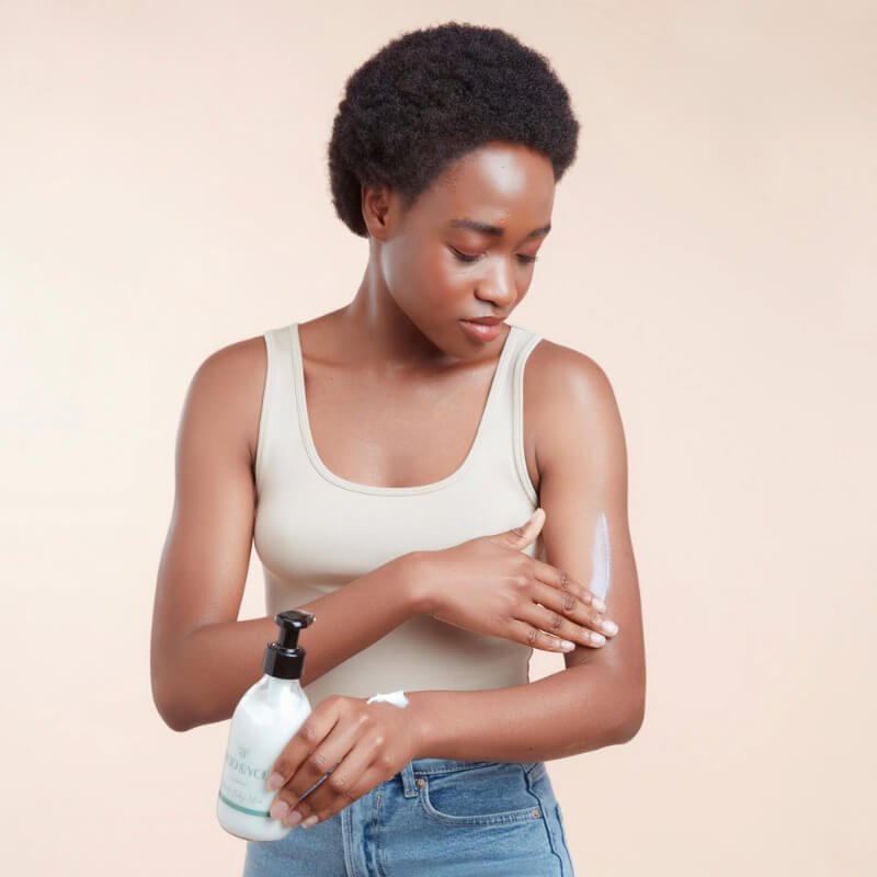 A woman applying Moo & Yoo miracle body lotion to her arm while holding the bottle