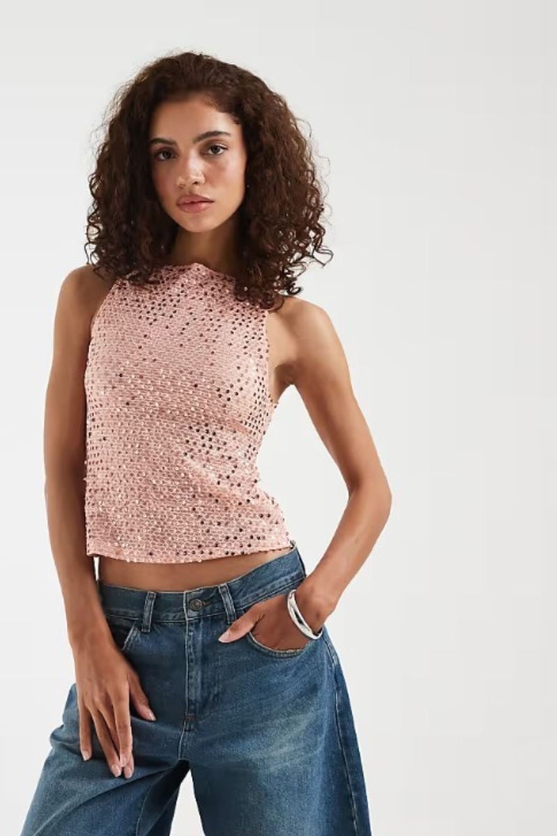 Model wearing Motel peach sequin knit top with halter neckline and wide-leg denim jeans