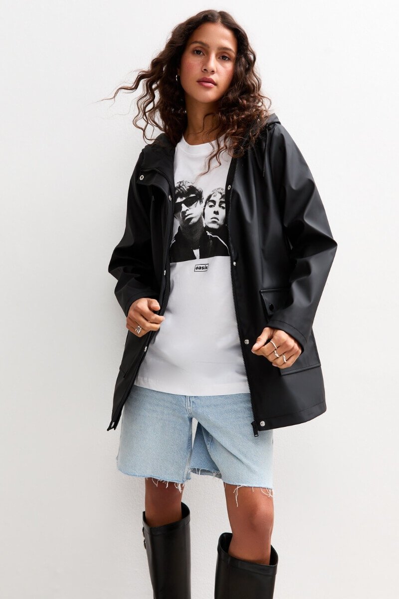 A person wearing New Look black water-resistant hooded anorak over a graphic tee and denim shorts, in a casual pose