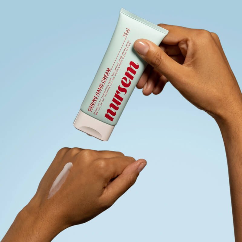 A hand applying Nursem Caring Hand Cream on another hand against a light blue background