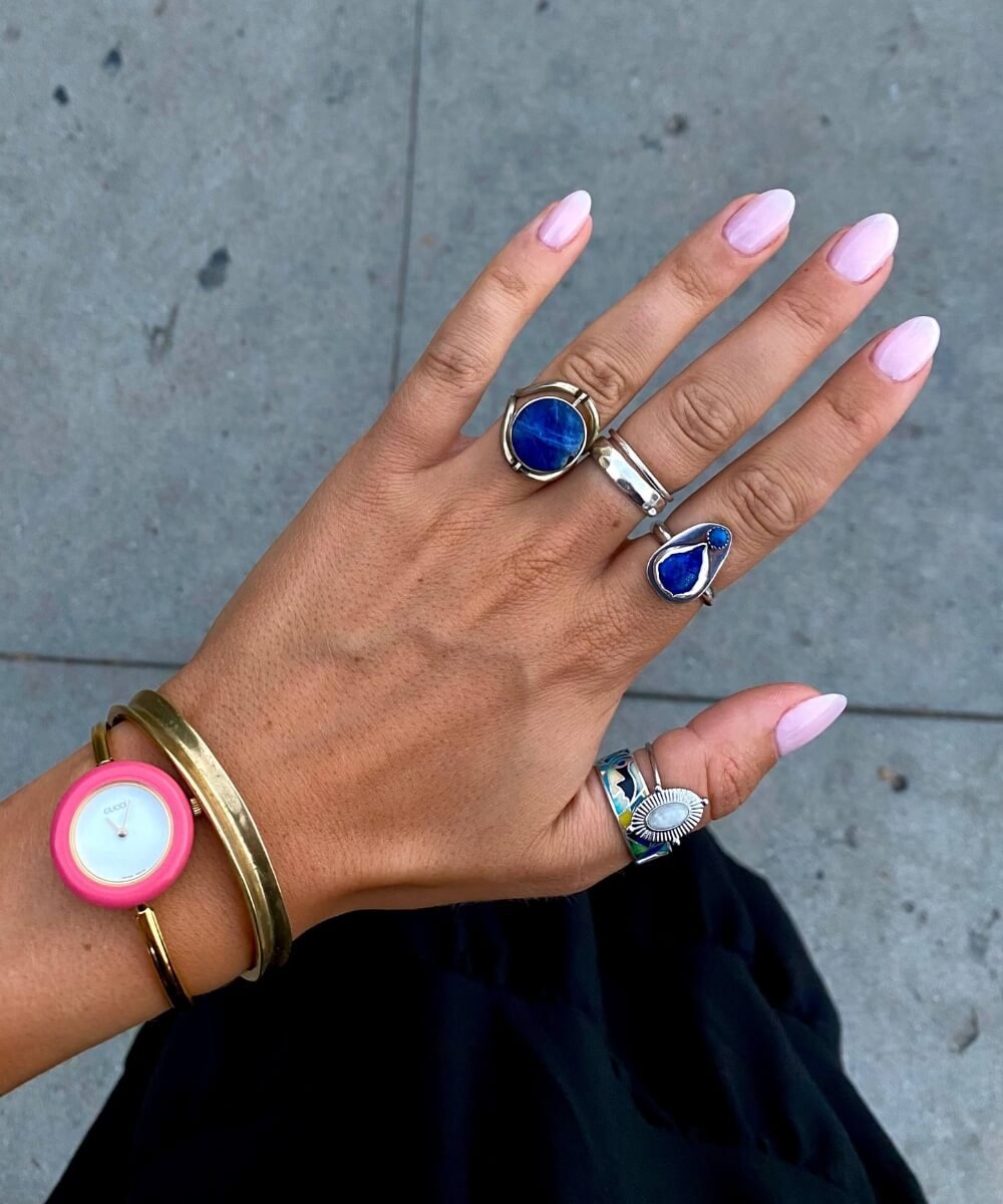 Glossy pastel pink almond-shaped spring nails styled with gold jewellery and statement rings