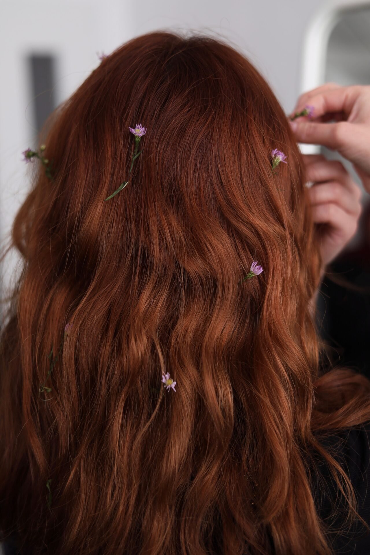 A person with long, wavy red hair adorned with small purple flowers
