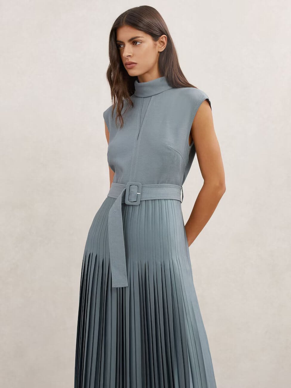 Model wearing Reiss Ania Roll-Neck Belted Pleated Midi Dress in Blue, a blue pleated midi dress with a roll neck and belt