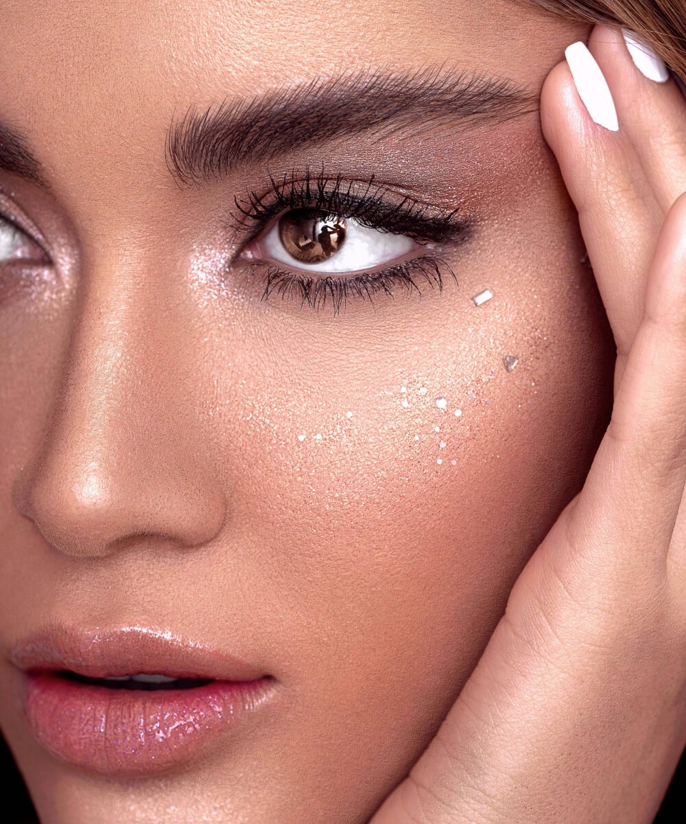 Close-up of a woman's eye with silver shimmer makeup and sparkling accents on her cheek