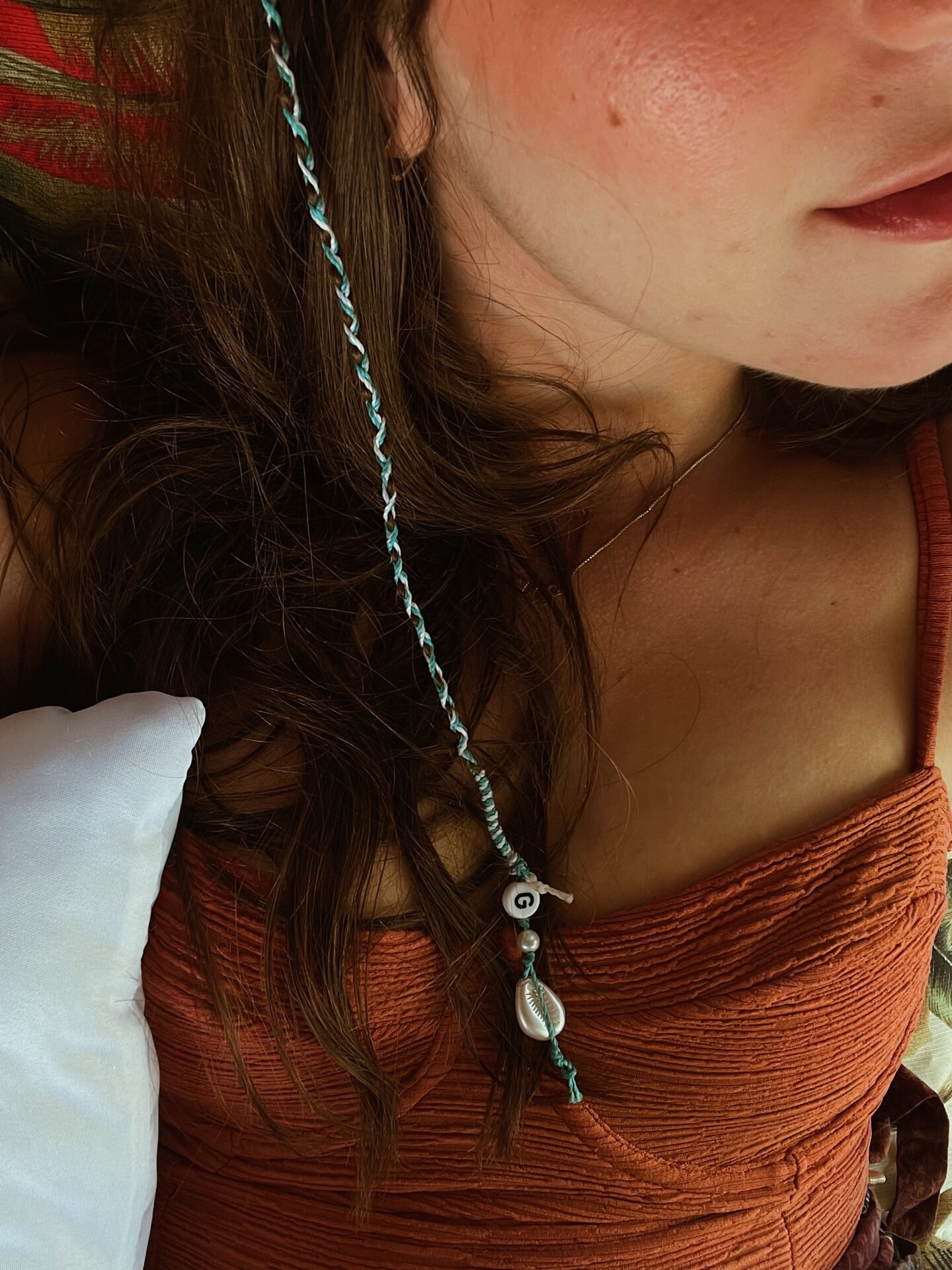 A close-up of a person's shoulder and neck, featuring wavy hair with a decorative braid adorned with small beads, and the person is wearing an orange top