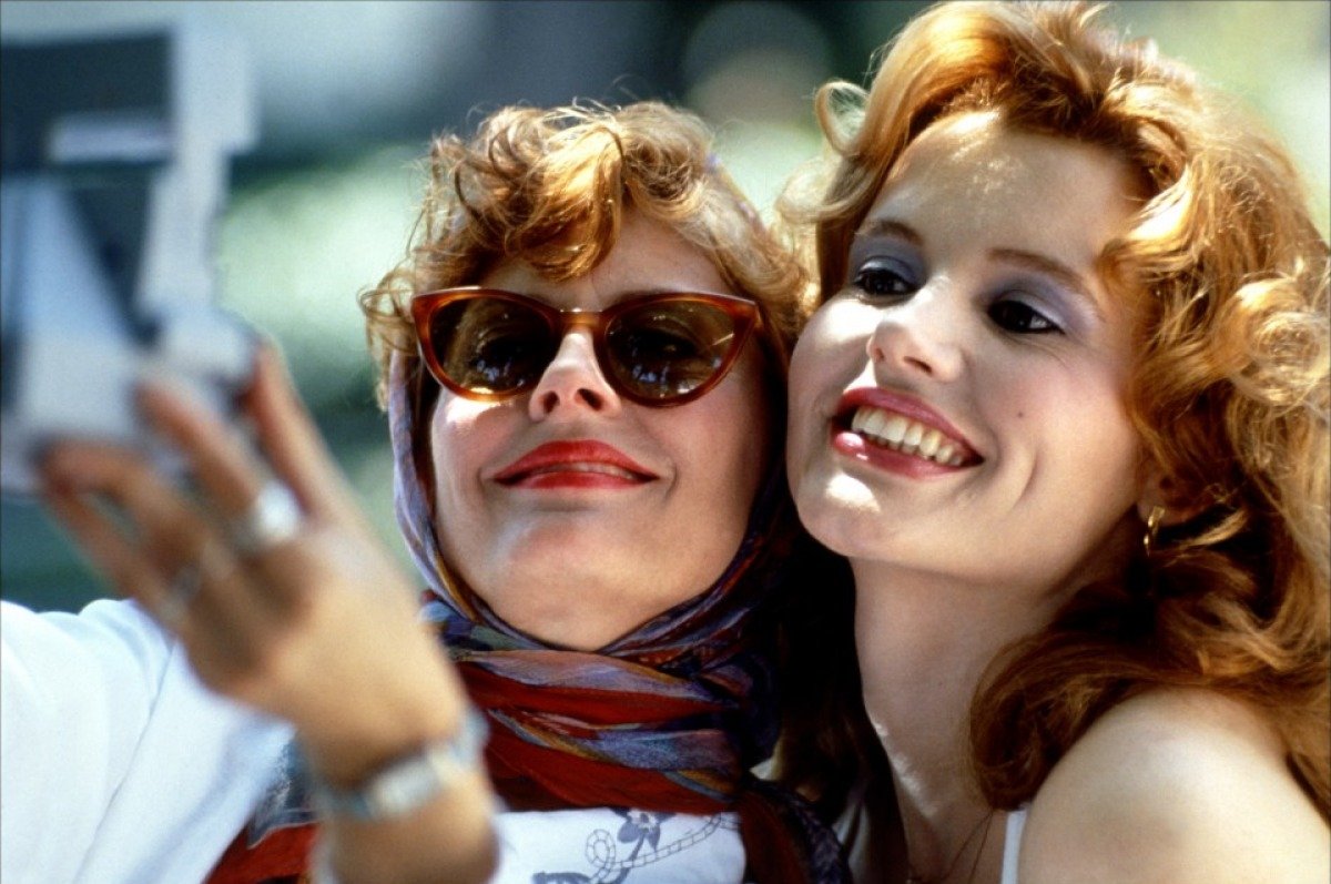 Susan Sarandon as Louise and Geena Davis as Thelma, smiling closely together as they take a selfie with a Polaroid camera in 'Thelma & Louise'.