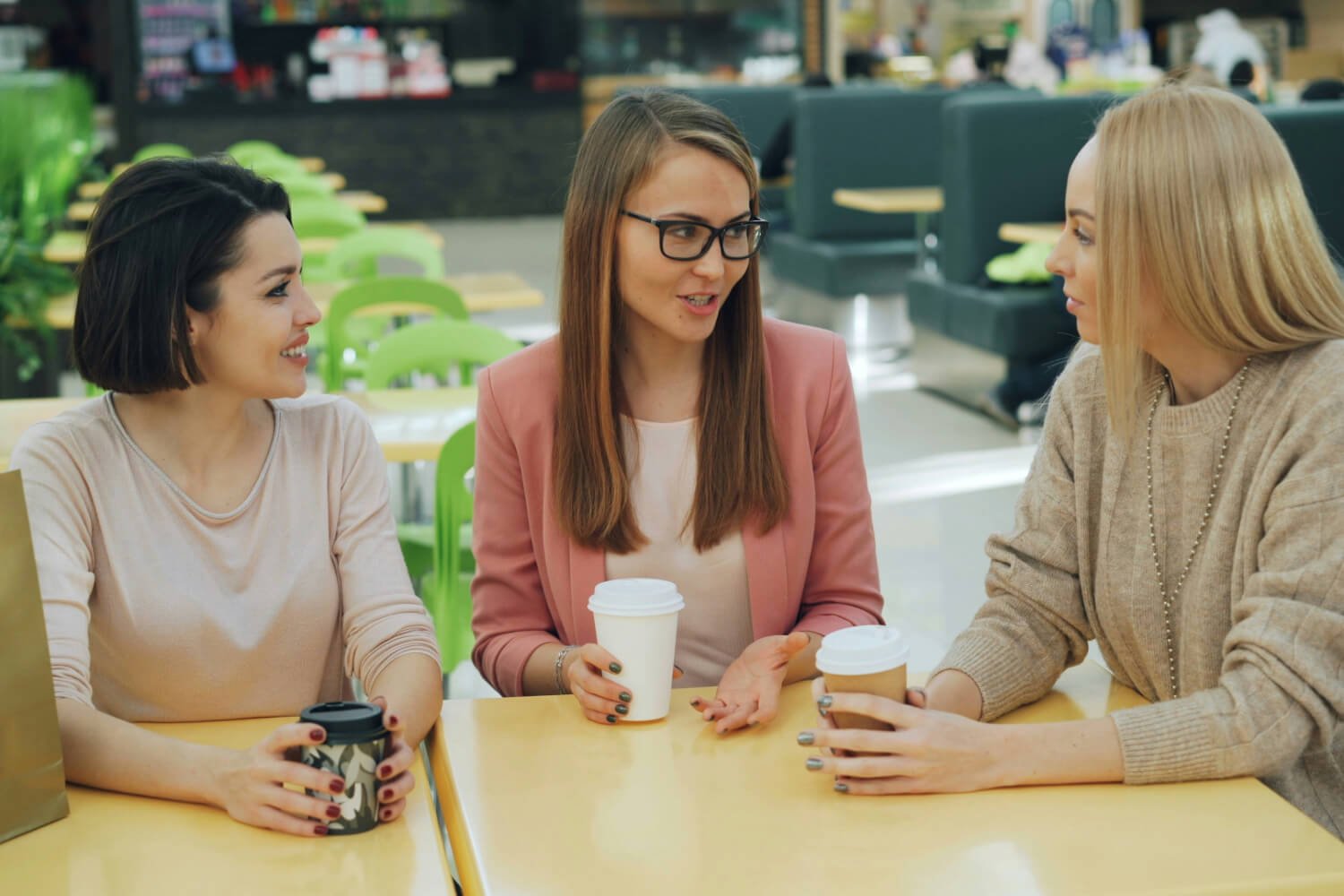 Three women friends chatting and drinking coffee together in a bright modern cafe
