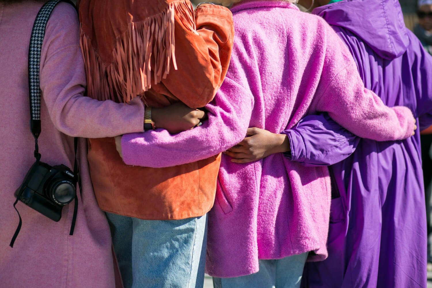 Four women standing together, wearing colourful jackets and holding each other warmly