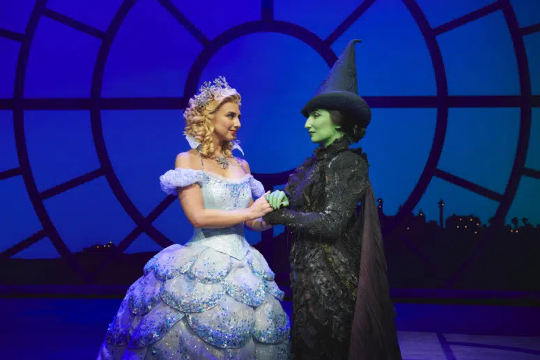 wicked the musical live on stage with green witch elphaba and good witch glenda, holding hands 