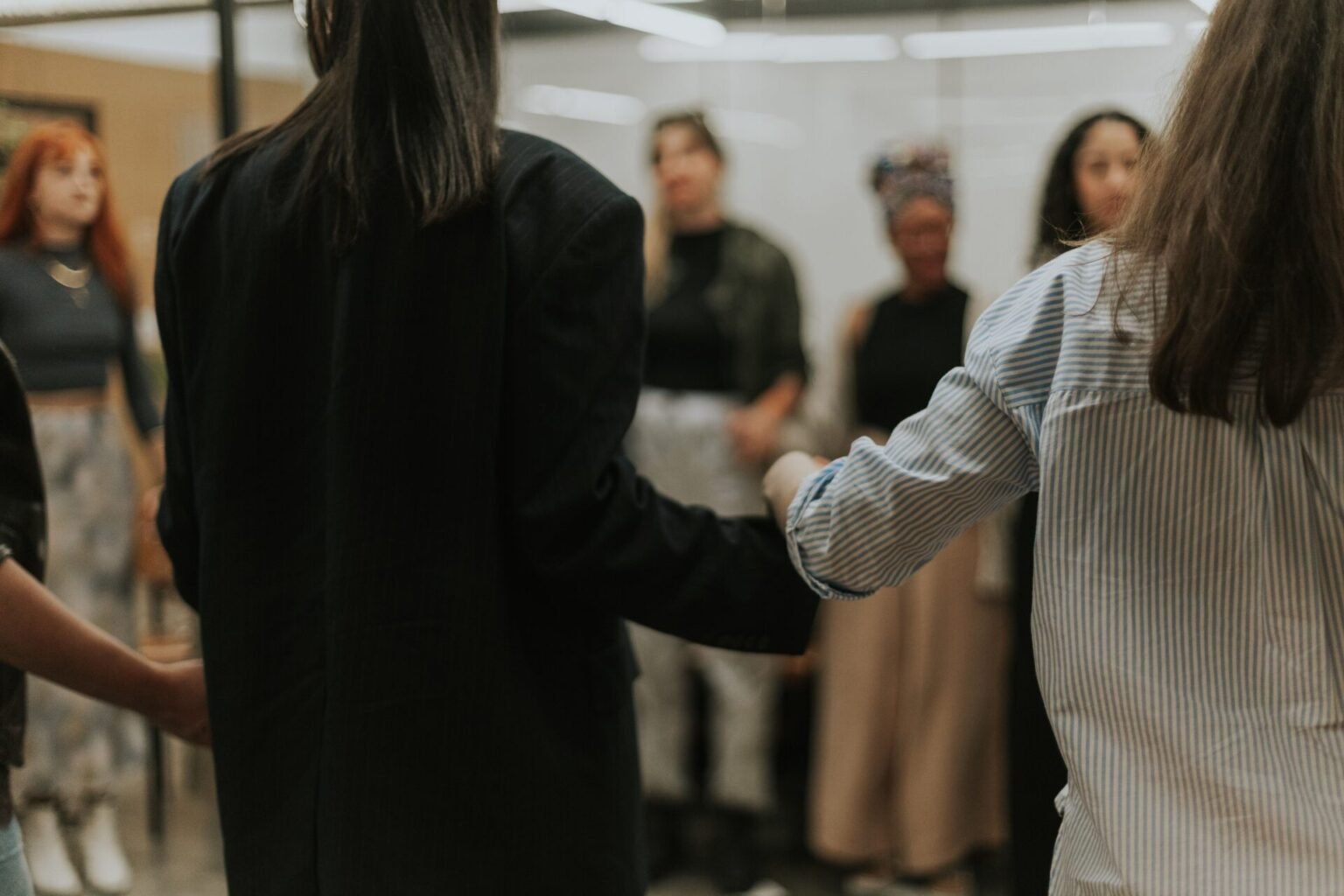 A group of women standing in a circle holding hands during a women-only club meeting, creating a safe social space for connection and community.