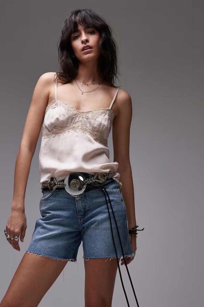 A model wearing Wrangler mid-wash blue cowboy shorts and a light silk camisole, posing confidently