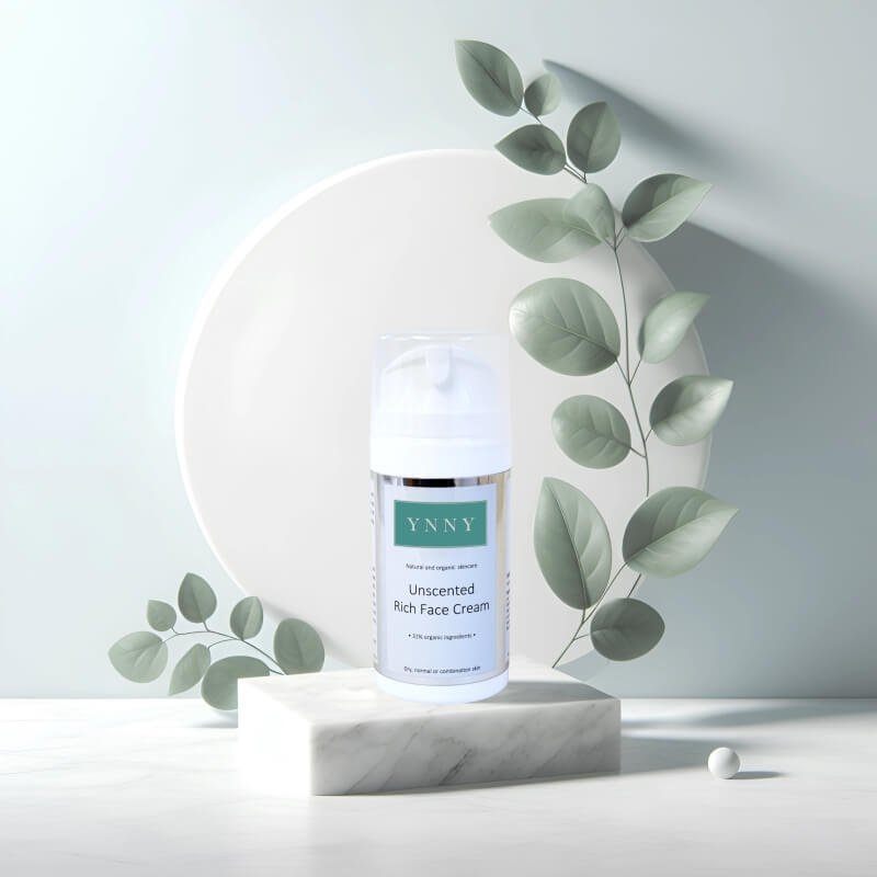 A bottle of YNNY unscented rich face cream on a marble pedestal with soft green leaves in the background